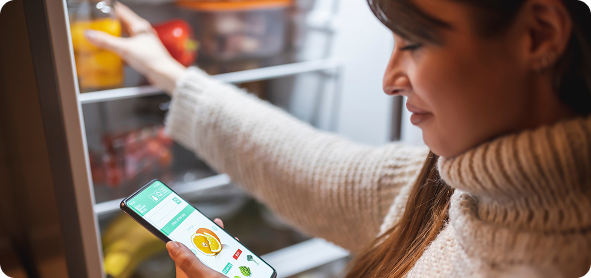 Woman checking her phone while reaching into the refrigerator
