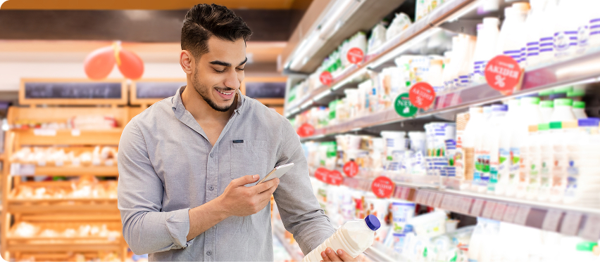 Shopper checking phone while holding milk in a grocery aisle